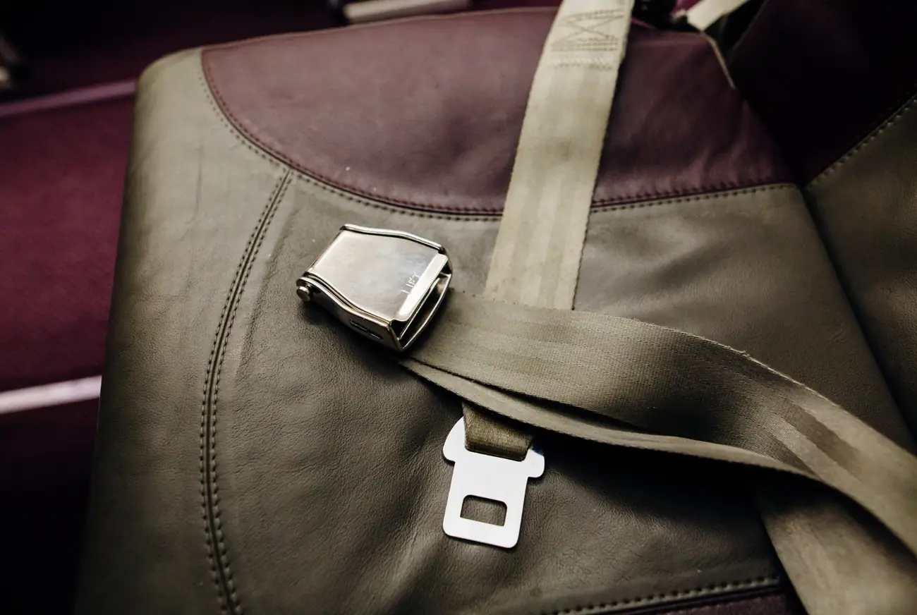 Seat belt webbing running across an upholstered seat towards a metal lift-latch buckle