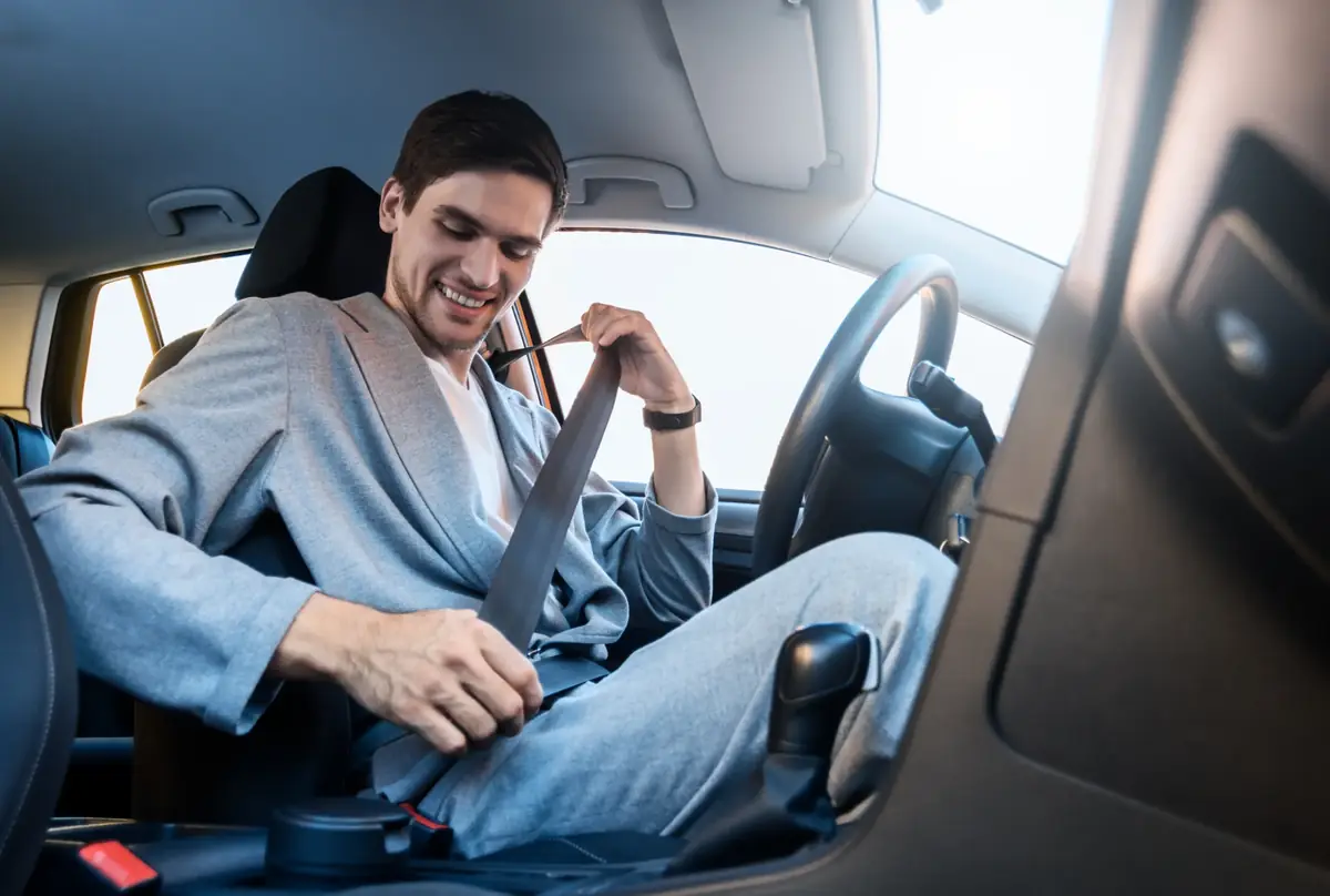Driver seated in a car drawing the seat belt across before setting off