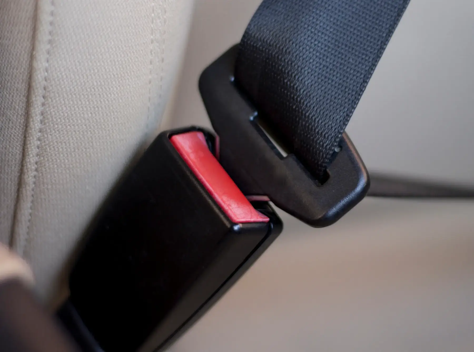 Close-up of an automotive seat belt tongue plate aligned with its buckle housing inside a vehicle interior