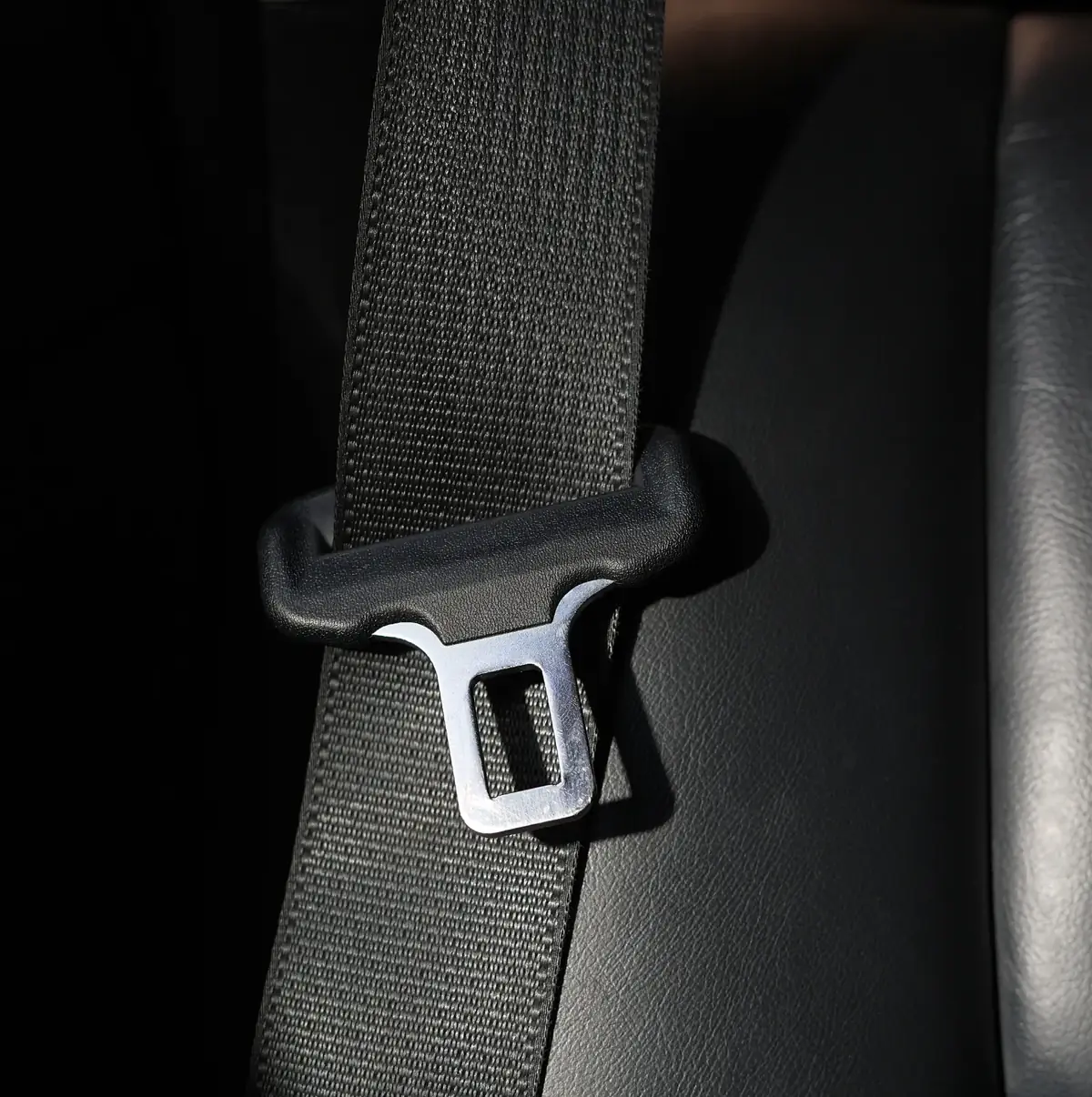 Seat belt webbing passing through a moulded pillar loop guide with its metal tongue plate resting alongside