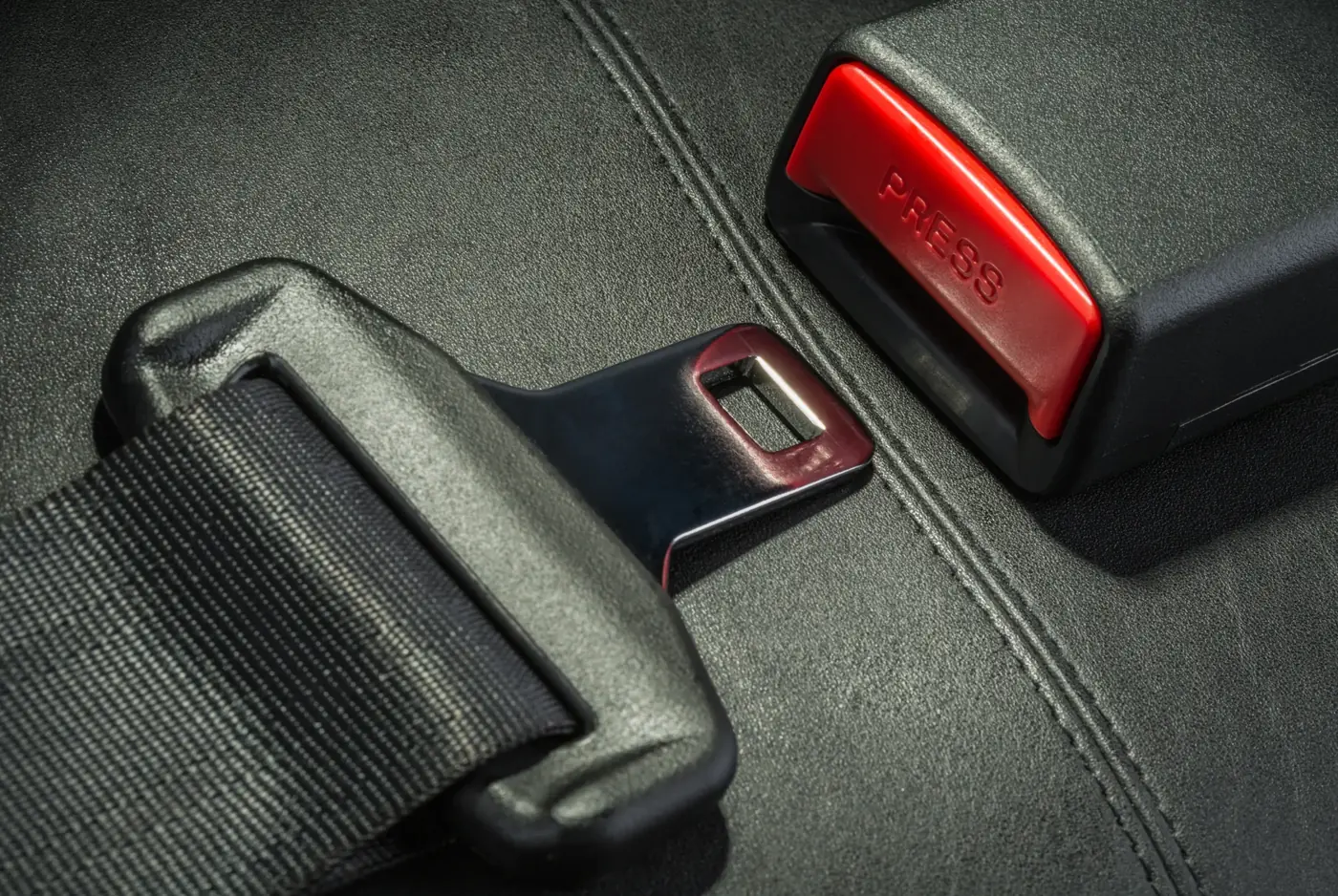 Detailed view of a seat belt latch plate and buckle release button on a dark automotive panel
