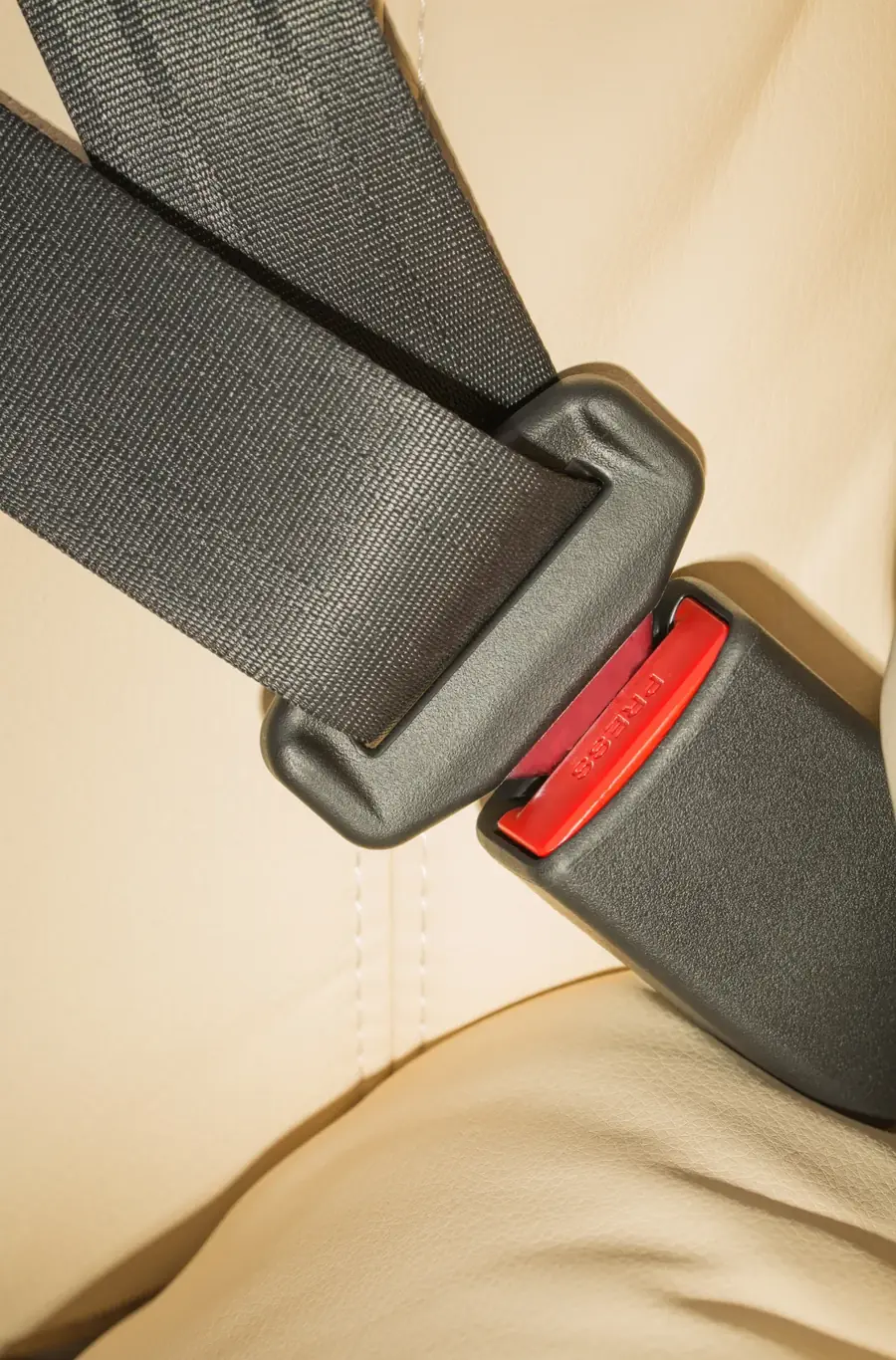 Seat belt assembly fastened across a light-coloured vehicle seat, viewed from above