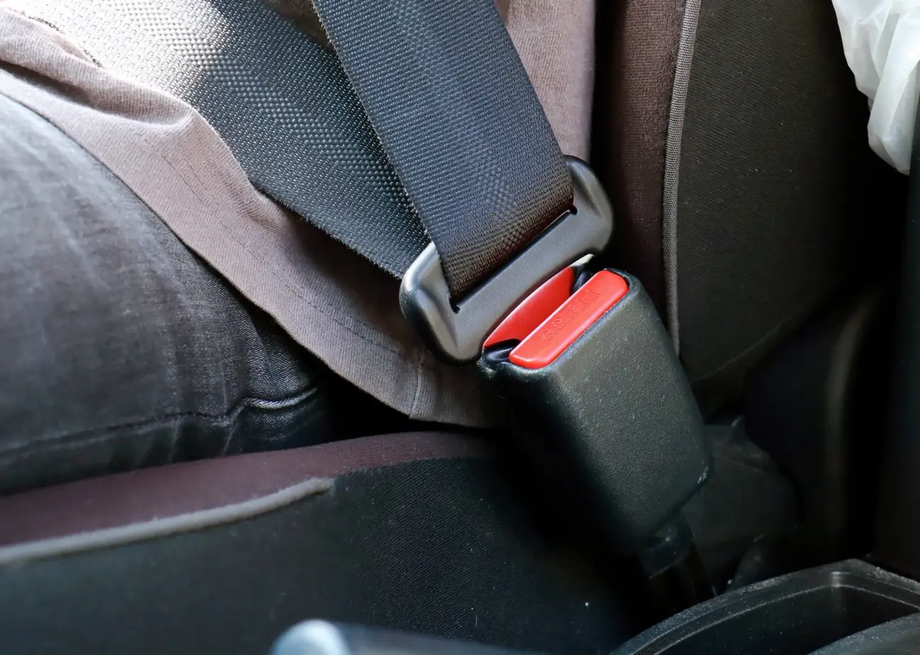 Metal seat belt latch plate held beside its buckle housing for inspection