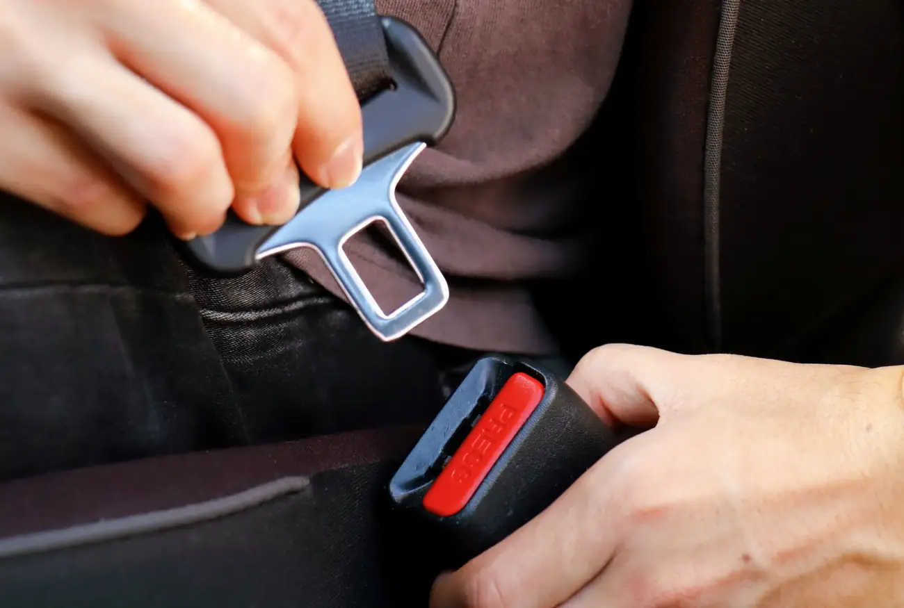 Hands aligning a seat belt tongue plate with its buckle housing